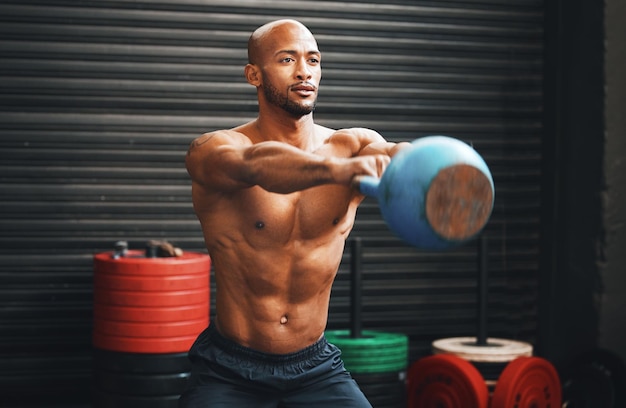 Generowanie mocy i siły przy każdym zamachu Ujęcie umięśnionego młodego mężczyzny ćwiczącego z kettlebell na siłowni