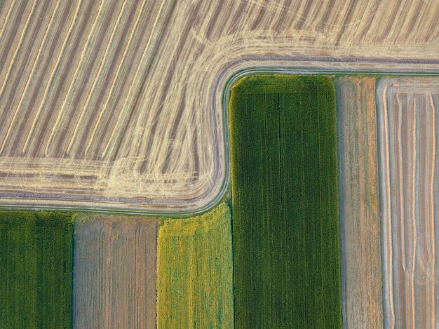 Geometryczne streszczenie tło pól uprawnych z różnymi uprawami i po zbiorach, oddzielone drogą. Widok z lotu ptaka z drona.