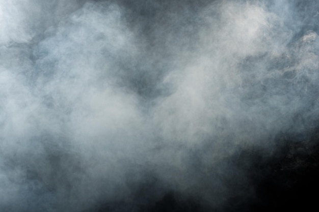 Gęste puszyste kłęby białego dymu i mgły na czarnym tle, abstrakcyjne chmury dymu, ruch nieostry. Palenie ciosów z suchej muchy maszyny i fruwające w powietrzu, efekt tekstury