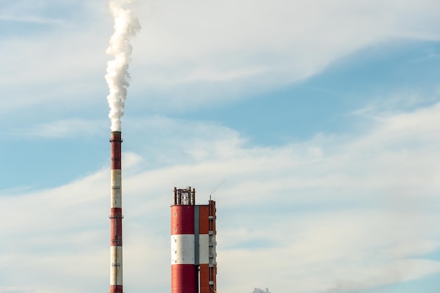Gęsty biały dym wydobywający się z dużej rury zakładu przemysłowego lub fabryki Dymiący komin na tle błękitnego nieba Zanieczyszczenie środowiska przedsiębiorstw chemicznych i farmaceutycznych