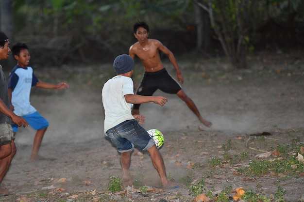 GILI ASAHAN, INDONEZJA - SIERPIEŃ, 22 2016 - chłopcy grają w piłkę nożną o zachodzie słońca na polu palmowym w pobliżu plaży