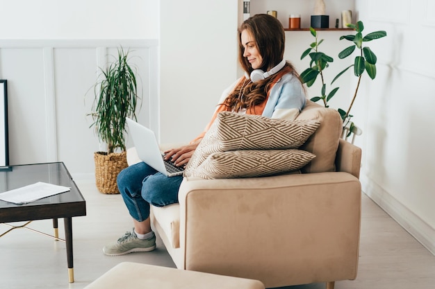 Ginger młoda freelancerka pracuje online w Internecie siedząc na kanapie w salonie