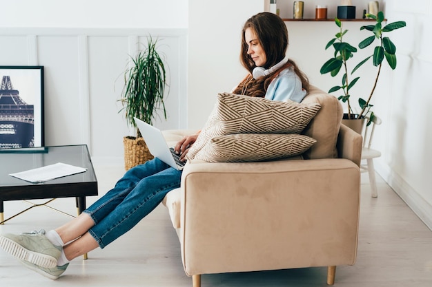 Ginger młoda freelancerka pracuje online w Internecie siedząc na kanapie w salonie