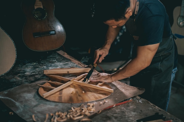 Gitarzyści azjatycki człowiek wytwarzający gitary akustyczne w laboratorium Azjatycki producent gitar buduje wysokiej jakości gitary dla muzyków ręcznie robiony sklep z gitarami Praca z piękną tradycją drzewną starożytne rzemiosło