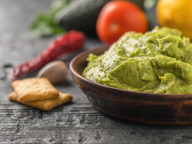 Zdjęcie gliniana miska ze świeżym guacamole, pomidorami, cytryną, frytkami i czosnkiem na drewnianym stole