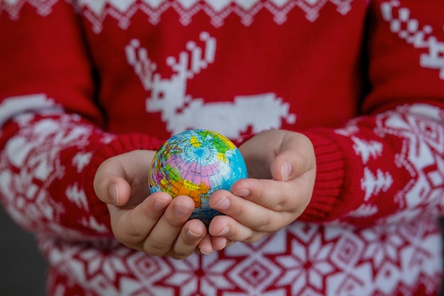 Zdjęcie glob w rękach dzieci w świątecznym swetrze. boże narodzenie koncepcja minimalizmu. wysokiej jakości zdjęcie