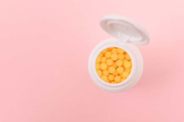 Globalny przemysł farmaceutyczny i produkty lecznicze - żółte witaminy lub tabletki w butelce leżącej na różowym tle. Miejsce kopiowania, widok z góry, układ płaski Flat