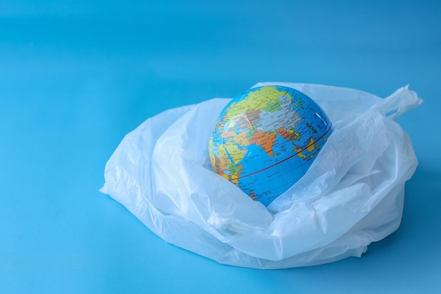 Globus w plastikowej torbie na niebieskim tle. Koncepcja ochrony świata przed plastikowymi odpadami