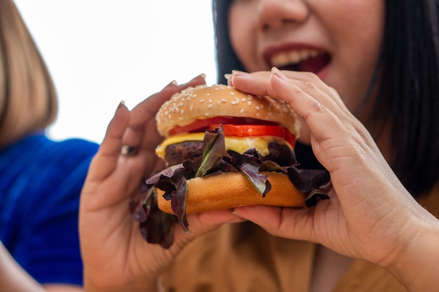 Zdjęcie głodna kobieta z nadwagą uśmiecha się i trzyma hamburgera i siedzi w salonie