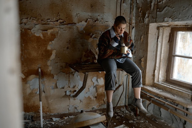 Głodna, przygnębiona, bezradna młoda kobieta jedząca przetwory z puszki, siedząca w opuszczonym pokoju i patrząca przez okno, czująca się zdesperowana
