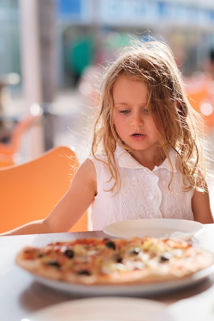 Głodne dziecko dziewczynka je pizzę na tarasie kawiarni w słoneczny dzień poza restauracją kopia przestrzeń pionowa