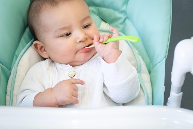 Głodne dziecko gryzie plastikową łyżkę przy stole na wysokim krześle Ząbkowanie kaprysy swędzące dziąsła wprowadzenie uzupełniających pokarmów