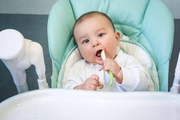 Głodne dziecko gryzie plastikową łyżkę przy stole na wysokim krześle Ząbkowanie kaprysy swędzenie dziąseł wprowadzenie uzupełniających pokarmów