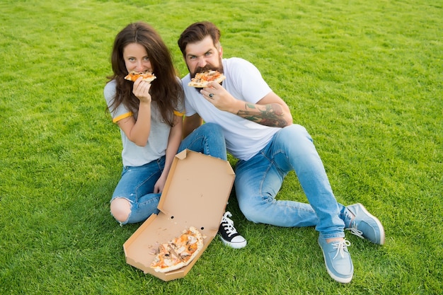 Głodni ludzie. Proste szczęście. Oszukany posiłek. Para jedzenie pizzy relaks na zielonym trawniku. Szybka dostawa żywności. Brodaty mężczyzna i dziewczyna jedzą tandetną pizzę. Zakochana para spotyka się na świeżym powietrzu z pizzą.