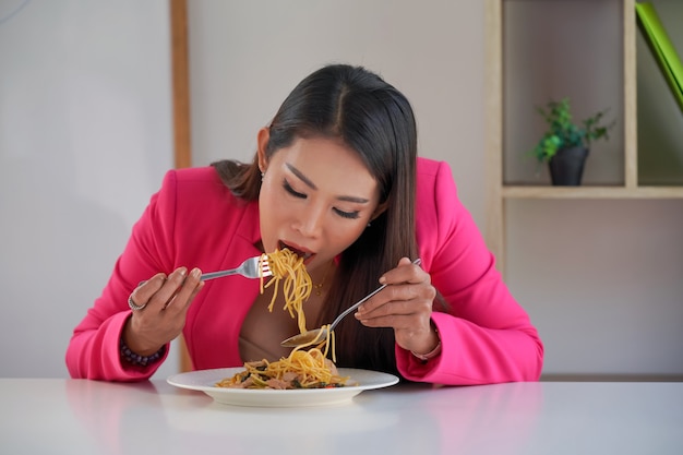 Głodny bizneswoman jedzenie spaghetti. Talerz makaronu i widelec dziko zjada makaron. Przedsiębiorcy lub pracownik biurowy o włoskie jedzenie w przerwie obiadowej.