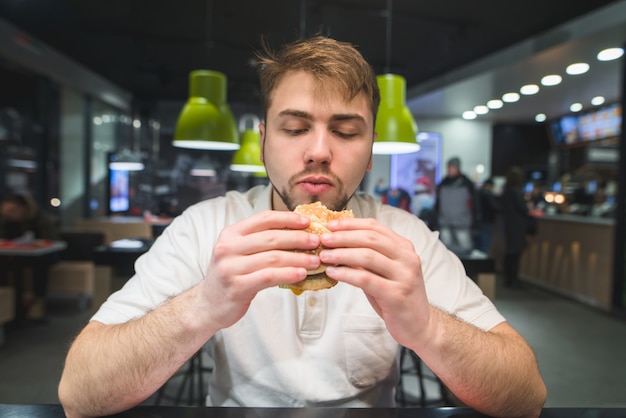 Głodny Człowiek Patrzy Na Kanapkę W Swoich Rękach. Mężczyzna Zje Wspaniałego Apetycznego Burgera