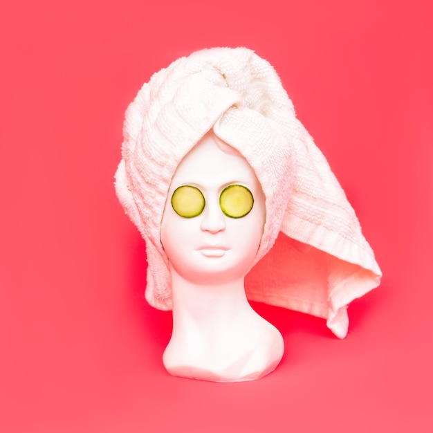 Głowa antycznej figurki kobiety z białym ręcznikiem po prysznicu i plastrami ogórka na oczach