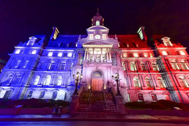 Zdjęcie główny budynek ratusza w starym montrealu oświetlony kolorami francji: niebieskim, białym i czerwonym