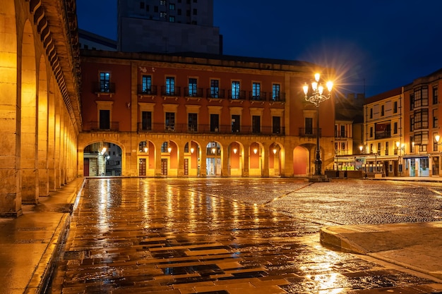 Główny plac turystycznego miasta Gijon nocą z monumentalnymi budynkami i łukami w arkadach Hiszpania