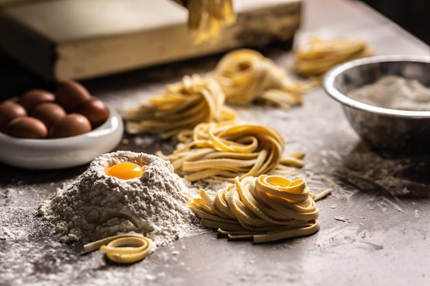 Gniazda świeżego makaronu fettuccine z jajkami, żółtkiem jaja, mąką na stole do przygotowania kuchni na stole do przygotowania kuchni.