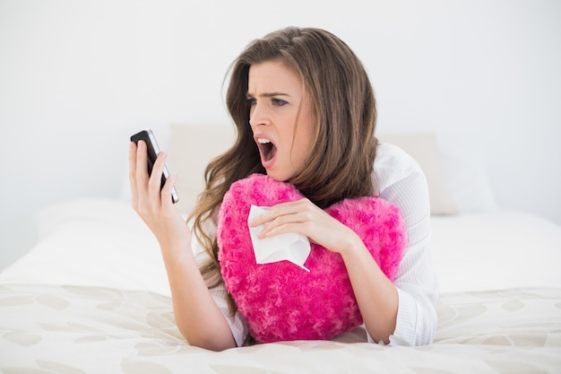 Gniewna przypadkowa brown z włosami kobieta wiesza w górę jej telefonu komórkowego w białych piżamach