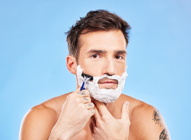 Golenie portretowe i brzytwa z modelem mężczyzny pielęgnującym w studio na niebieskim tle w celu odnowy biologicznej lub pielęgnacji Skóra twarzy i golenie z przystojnym młodym mężczyzną w łazience do usuwania zarostu