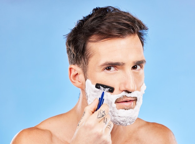 Golenie twarzy i brzytwa portret mężczyzny do higienicznego czyszczenia i rutyny samopielęgnacji dla zdrowej skóry Zdrowie odnowy biologicznej i twarz modelu z pianką do brody na makiecie niebieskiego studia do reklamy