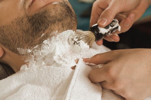 Golenie w zakładzie fryzjerskim. Zbliżenie strzelał fryzjer męski stosuje niektóre golenie śmietankę przed golić szyję jego klient