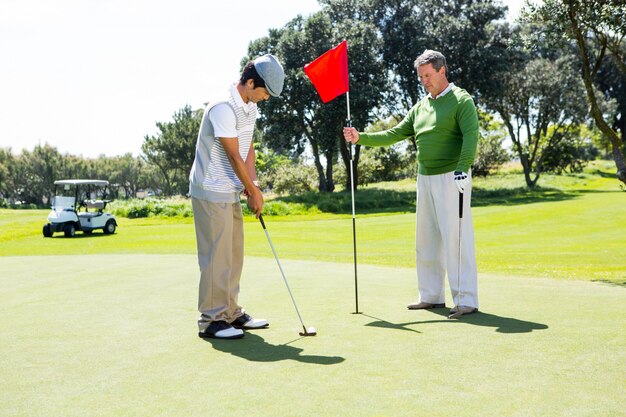 Golfista trzyma dziurę flaga dla przyjaciela kładzenia piłki