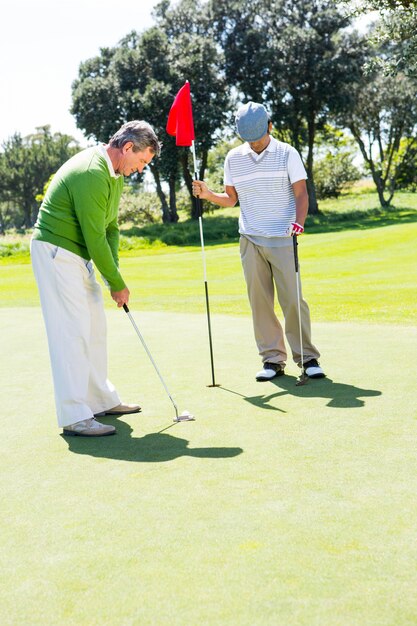 Golfista trzyma dziurę flaga dla przyjaciela kładzenia piłki