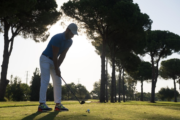 golfista uderzając strzał z klubem na kursie w piękny poranek z rozbłyskiem słońca w tle