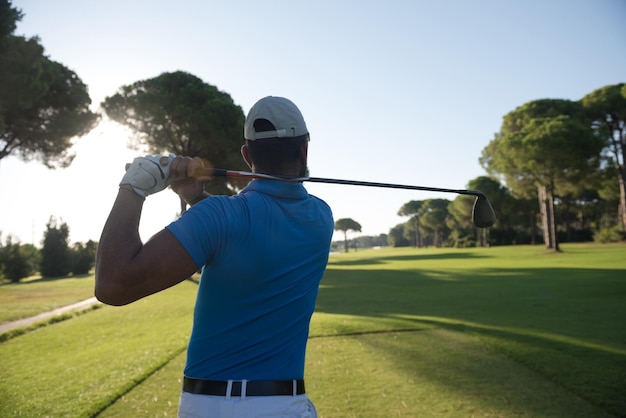 golfista uderzając strzał z klubem na kursie w piękny poranek z rozbłyskiem słońca w tle
