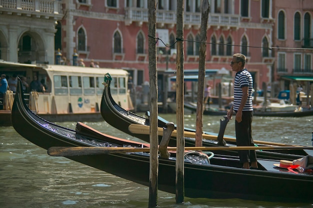 Gondolier czeka na swój kolejny wyścig nad swoją gondolą zacumowaną przy pomoście.