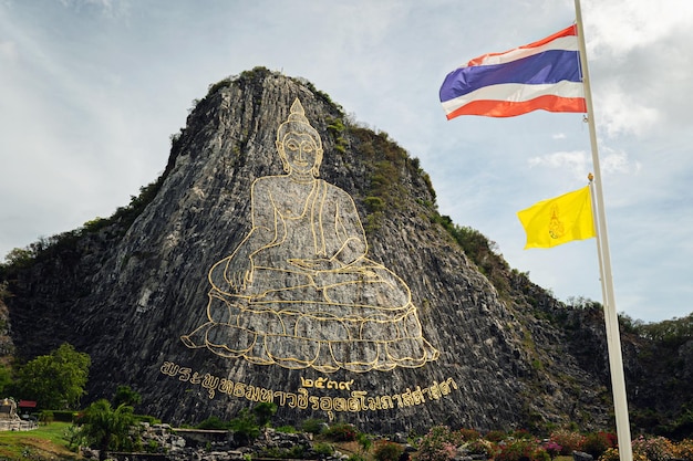 Góra Buddy Khao Chi Chan Sattahip Dystrykt Chon Buri Tajlandia Atrakcje religijne w okolicach Pattaya Złoty wizerunek Buddy na skale i flaga Tajlandii na tle pochmurnego nieba