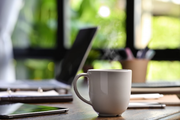 Gorąca i parująca filiżanka kawy na biurku z laptopem i gadżetem podczas pracy w domu