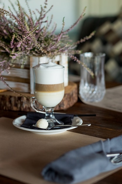 Gorąca kawa latte macchiato z smaczną pianką z przezroczystego szkła na ciemnym drewnianym stole z ciastkiem, cukrem trzcinowym. Czas na kawę, pyszny słodki napój. Czas na śniadanie. Retro stonowany obraz. Niski klucz ciemne zdjęcie.