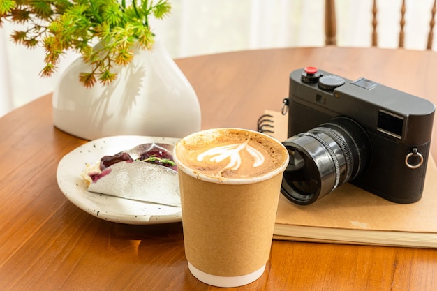 Gorąca Kawa Latte Z Pianką Mleczną Latte Art W Filiżance Wykonanej Z Papieru I Aparatu W Notatniku Ciasto Jagodowe Na Drewnianym Biurku Na Widoku Z Góry Jako śniadanie W Kawiarni W Kawiarnipodczas Koncepcji Pracy Biznesowej