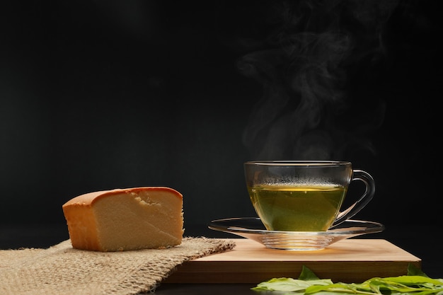 Zdjęcie gorąca zielona herbata w szklanym kubku z dymem i maślanym ciastem na desce.