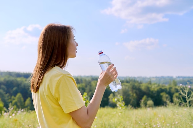 Zdjęcie gorące słoneczne lato spragniona dorosłej kobiety pijącej wodę z butelki do nas w przyrodzie