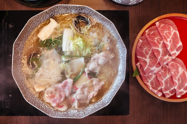 Gorący i gotujący się rosół Shabu z kapustą, eryngii, enotitake, tofu i wieprzowiną Kurobuta w gorącym garnku.