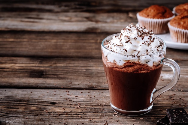 Gorący napój czekoladowy z bitą śmietaną w szklance na drewnianym rustykalnym tle