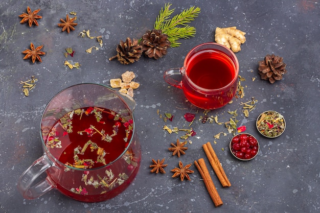 Gorący napój świąteczny. Czerwona herbata (rooibos, hibiskus, karkade) w szklanym kubku i czajniczku na świąteczną ucztę wśród żurawiny, pomarańczy, szyszek, cynamonu. Ferie zimowe, koncepcja nowego roku. Ścieśniać