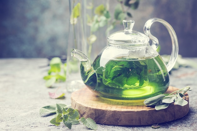 Gorący ziołowy napój herbaciany o działaniu uspokajającym w szklanym czajniczku na drewnianej tacy ze świeżą miętą ogrodową