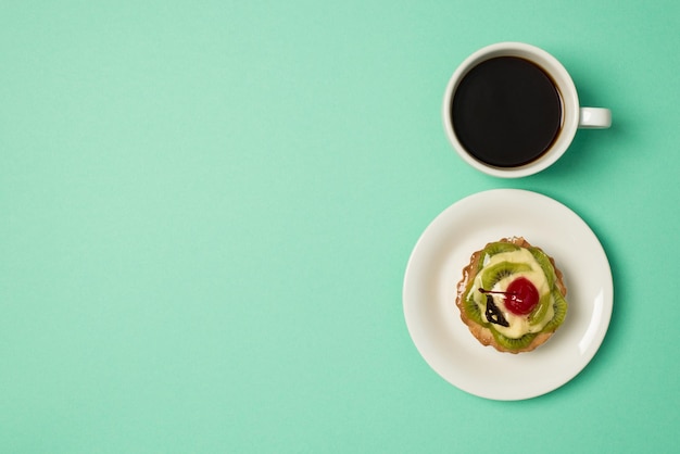 Górne zdjęcie filiżanki kawy i talerza z ciastem owocowym na tle turkusowym z copyspace
