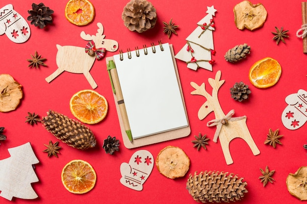 Górny widok notebooka na czerwonym tle ozdobiony świątecznymi zabawkami i symbolami Bożego Narodzenia reniferami i drzewami noworocznymi Koncepcja wakacyjna