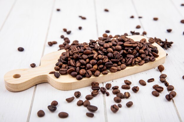 Górny widok świeżo pieczonych ziaren kawy na drewnianej desce kuchennej na białym drewnianym tle