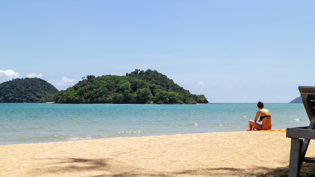 Górska wyspa nad morzem z turystą usiąść na plaży po prawej stronie z jasnym niebem