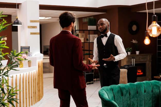 Gość i boy hotelowy dyskutują w holu, pytając o lokalne rekomendacje podczas wizyty w podróży służbowej. Pracownik umysłowy witany przez boya hotelowego w hotelu, luksusowe usługi.