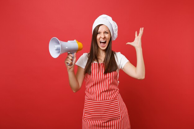 Gospodyni domowa kobieta kucharz lub piekarz w pasiasty fartuch t-shirt toczek kucharzy kapelusz na białym tle na tle czerwonej ściany. Zszokowana kobieta krzyczy w megafonie, zapowiada wyprzedaż. Makieta koncepcja przestrzeni kopii.