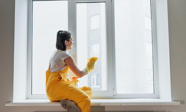 Gospodyni domowa w żółtym mundurze myjąca okna Koncepcja remontu domu